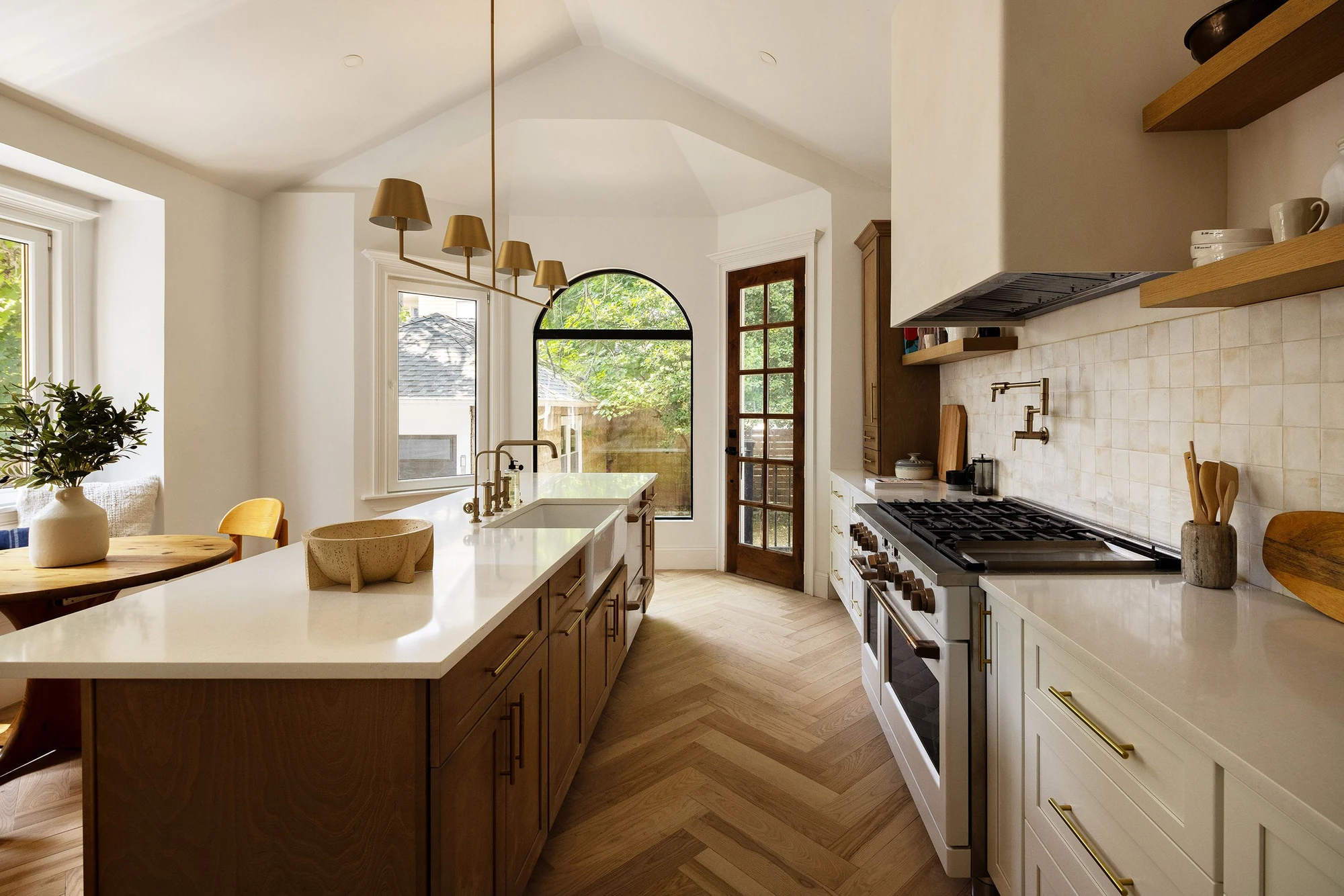 Kitchen with a central island, wood cabinetry, herringbone floor, and an arched window over a built-in breakfast area at 534 East 24th Street