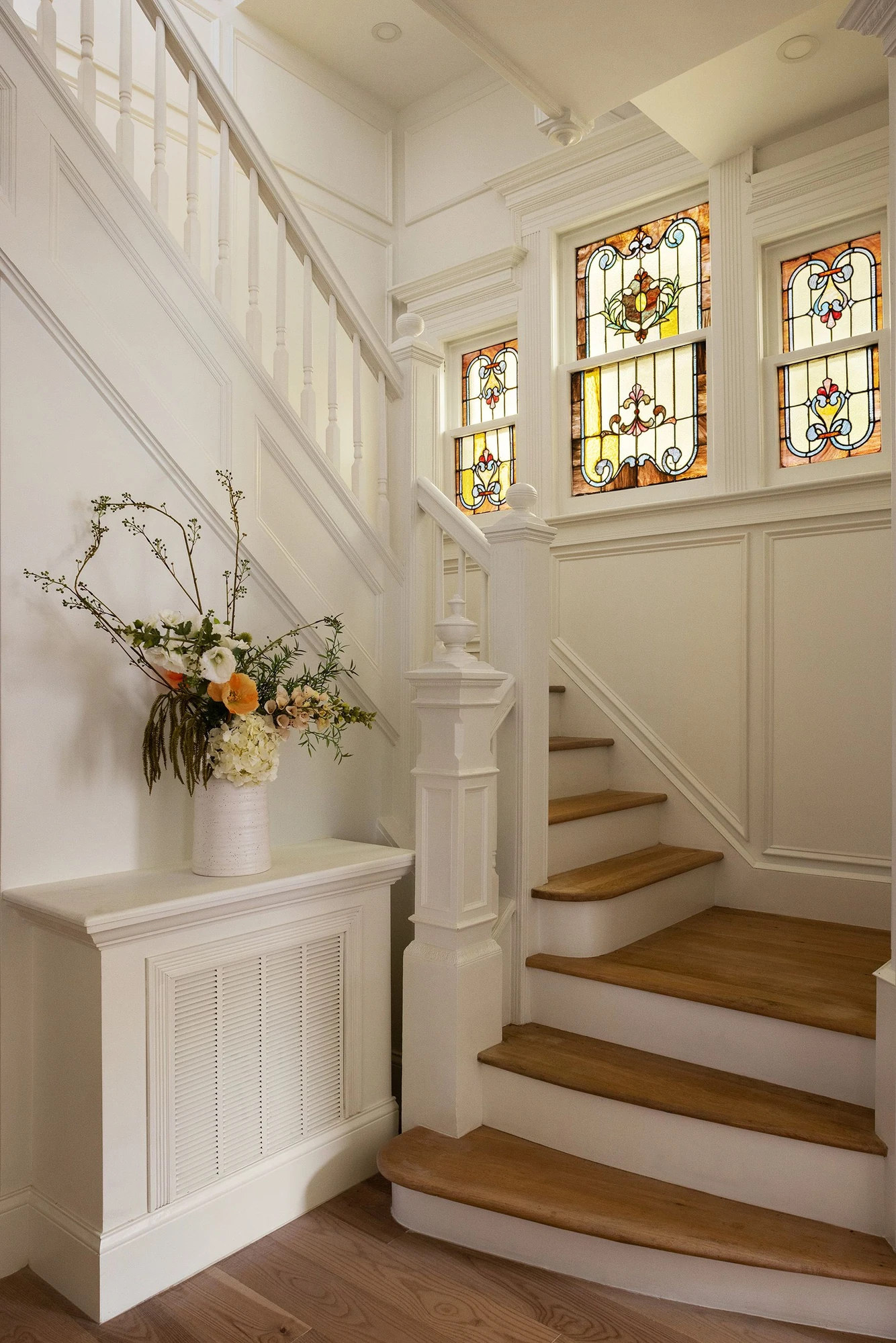 Staircase with stained glass windows, white wainscoting, and wood treads at 534 East 24th Street