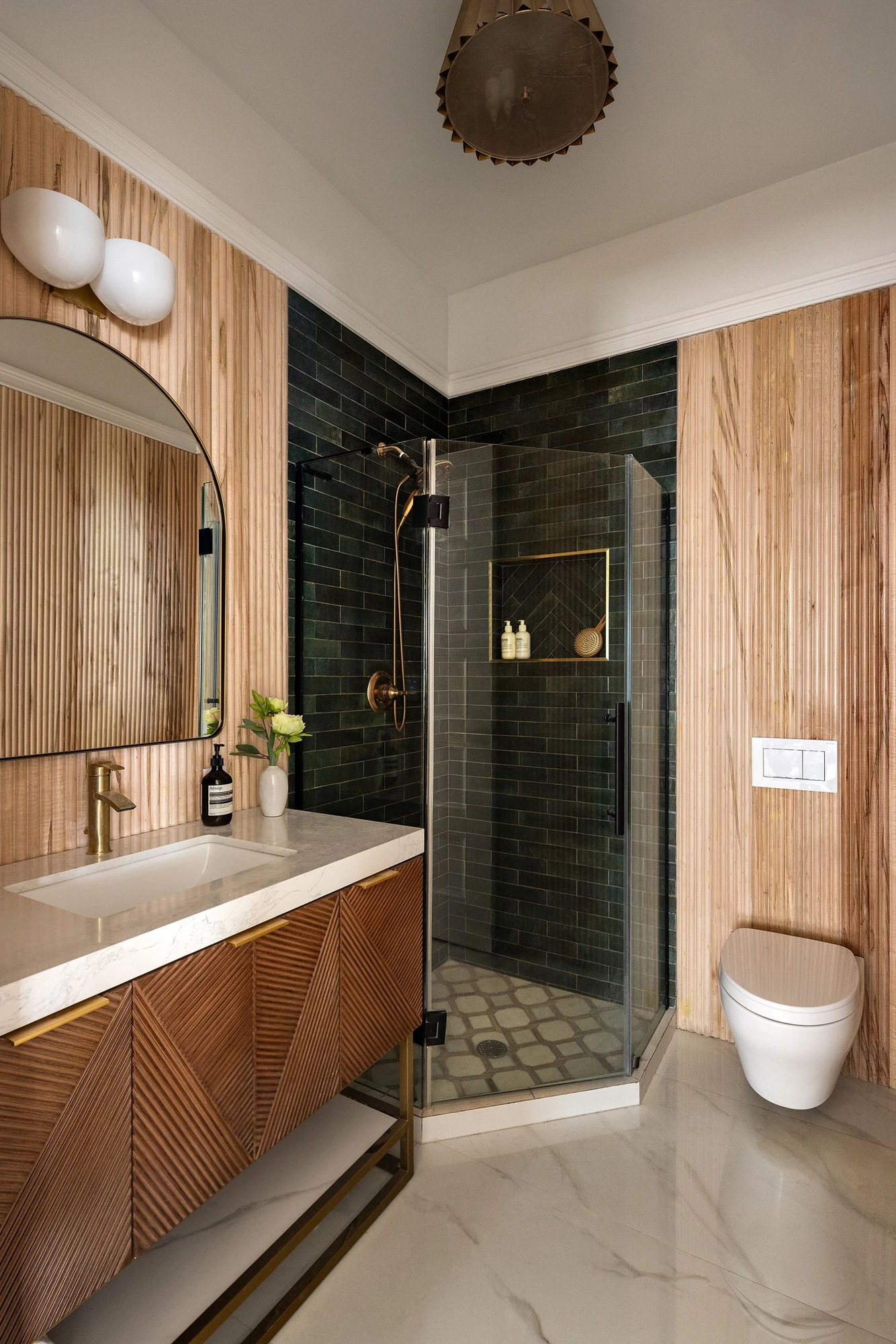 Bathroom with reeded wood paneling, a dark subway-tile shower, marble surfaces, and brass fixtures at 534 East 24th Street
