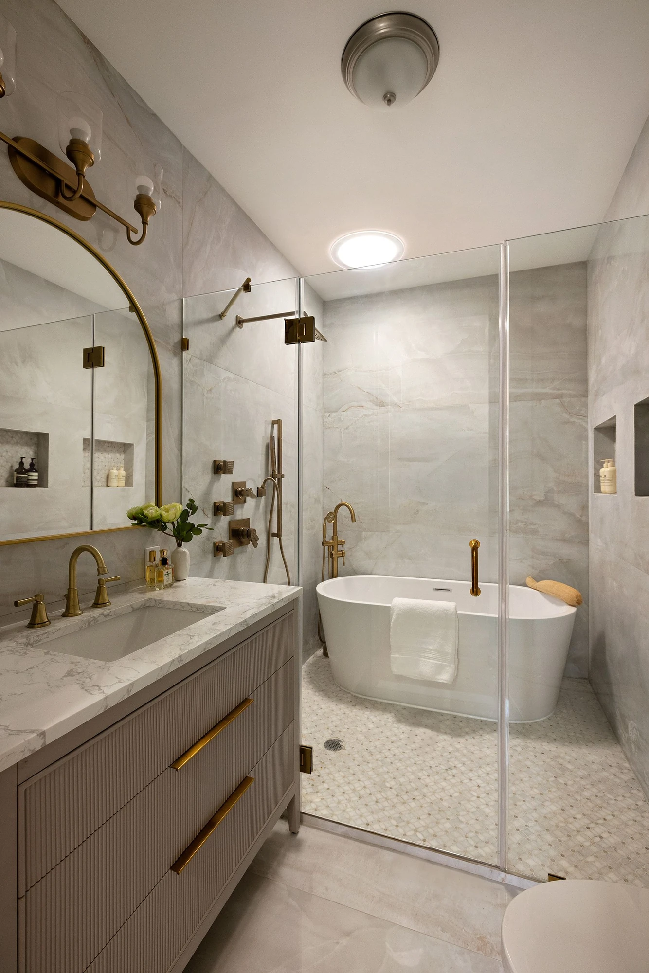 Pale marble bathroom with a freestanding tub, multijet shower, ribbed vanity, and brass fixtures at 534 East 24th Street