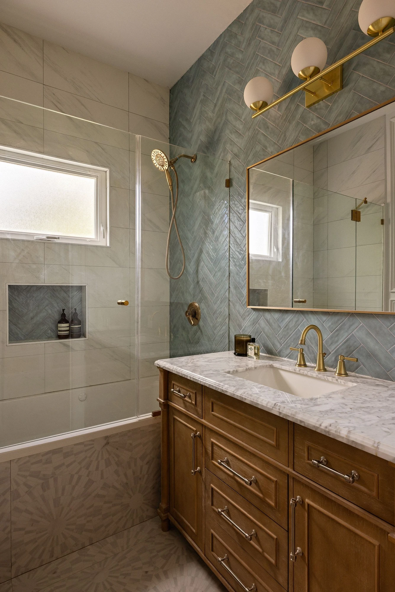 Bathroom with a blue-green herringbone tile wall, wood vanity, marble counter, and brass fixtures at 534 East 24th Street