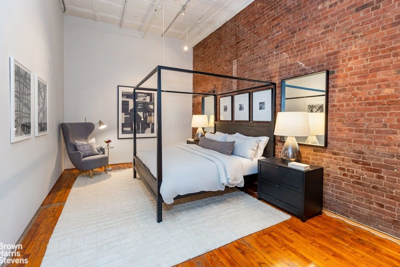 Sleeping area with a dark bed frame against a tall red-brick wall at 39 Worth Street