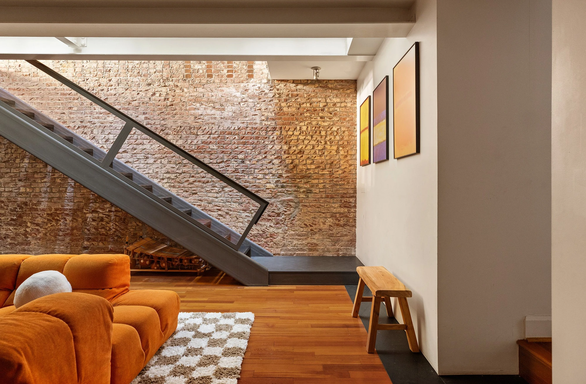 Metal staircase beside exposed brick and an orange sofa beneath a skylight at 62 Beach Street