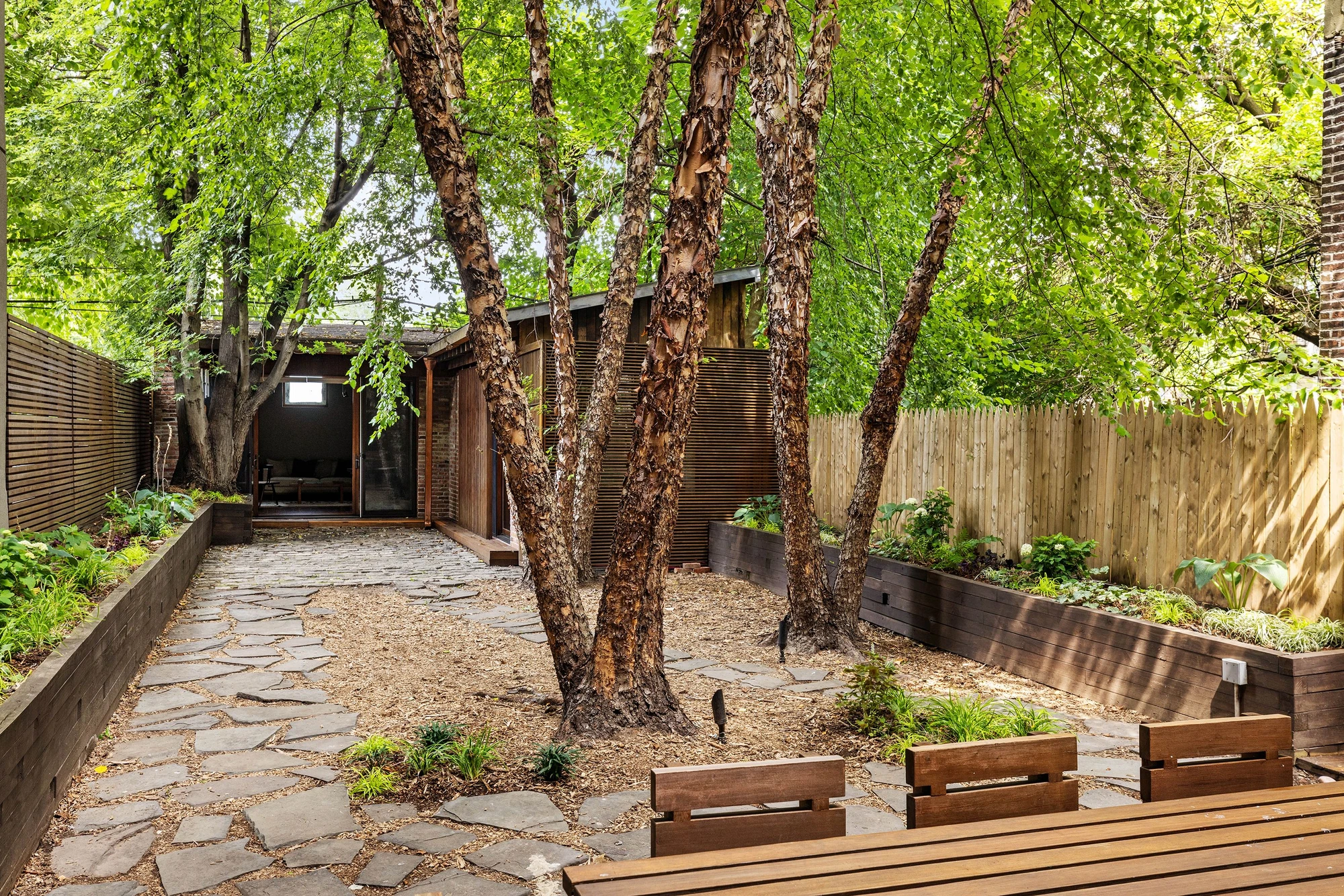 Leafy garden with a stone patio behind 497 Saint John's Place