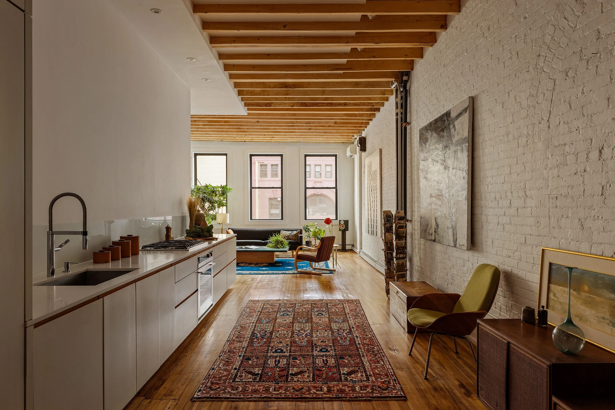 Long white-painted brick wall beside an open kitchen beneath wood ceiling beams at 62 Washington Avenue