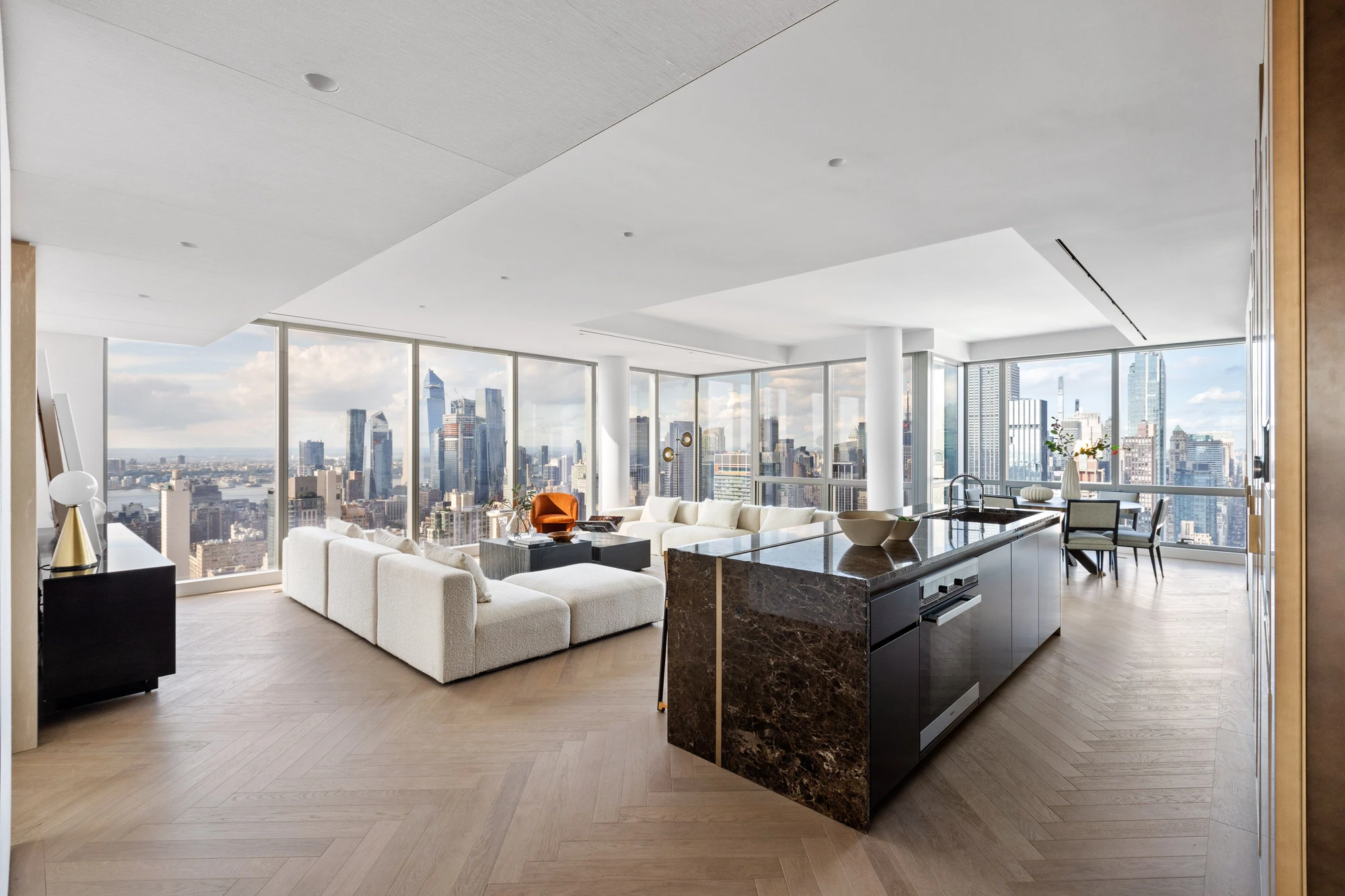 Daylight view across the open living room and dark stone kitchen island, with windows wrapping around two sides at One Madison 55B