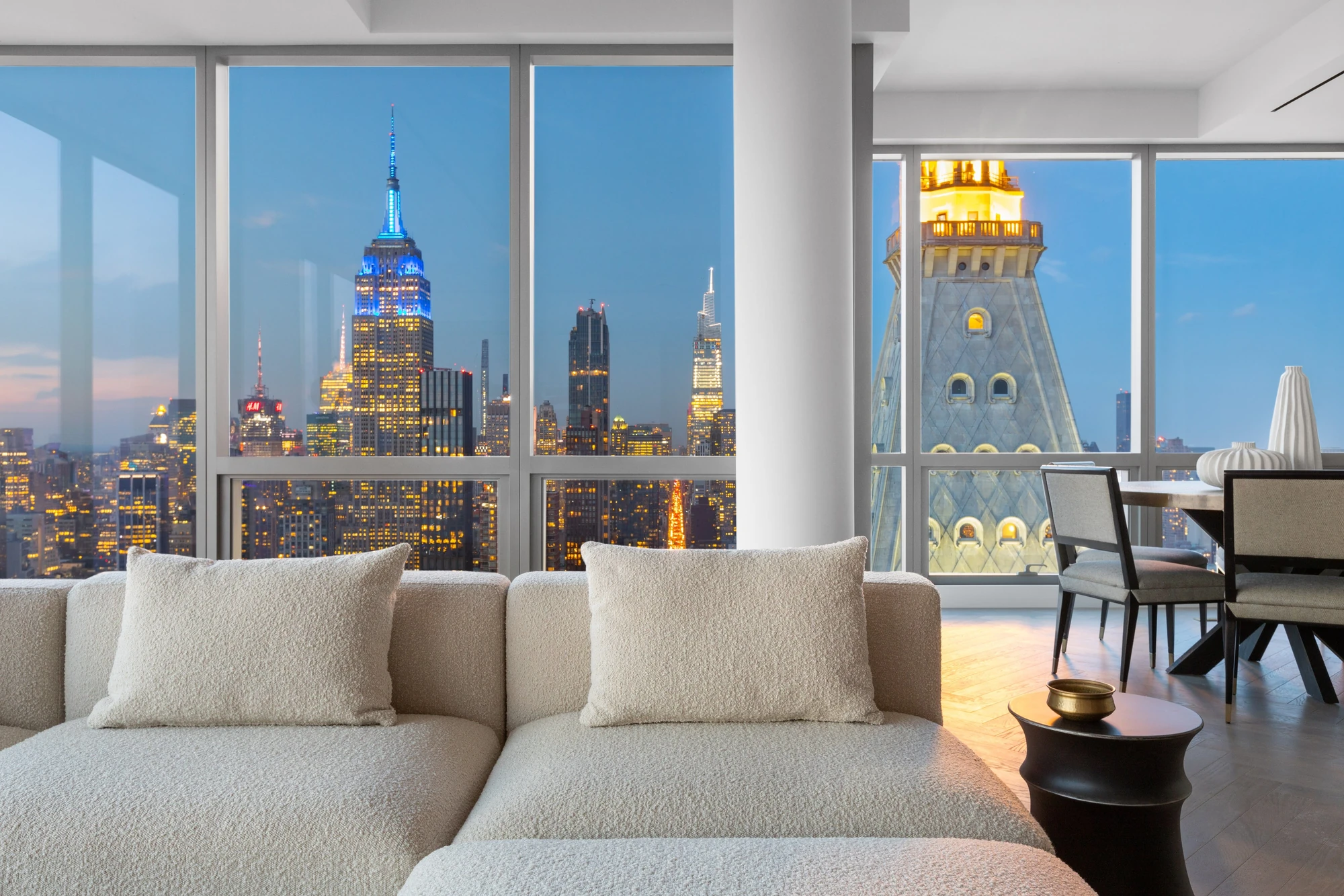 Twilight living and dining space at One Madison 55B, with the illuminated Empire State Building and MetLife Clock Tower beyond the windows