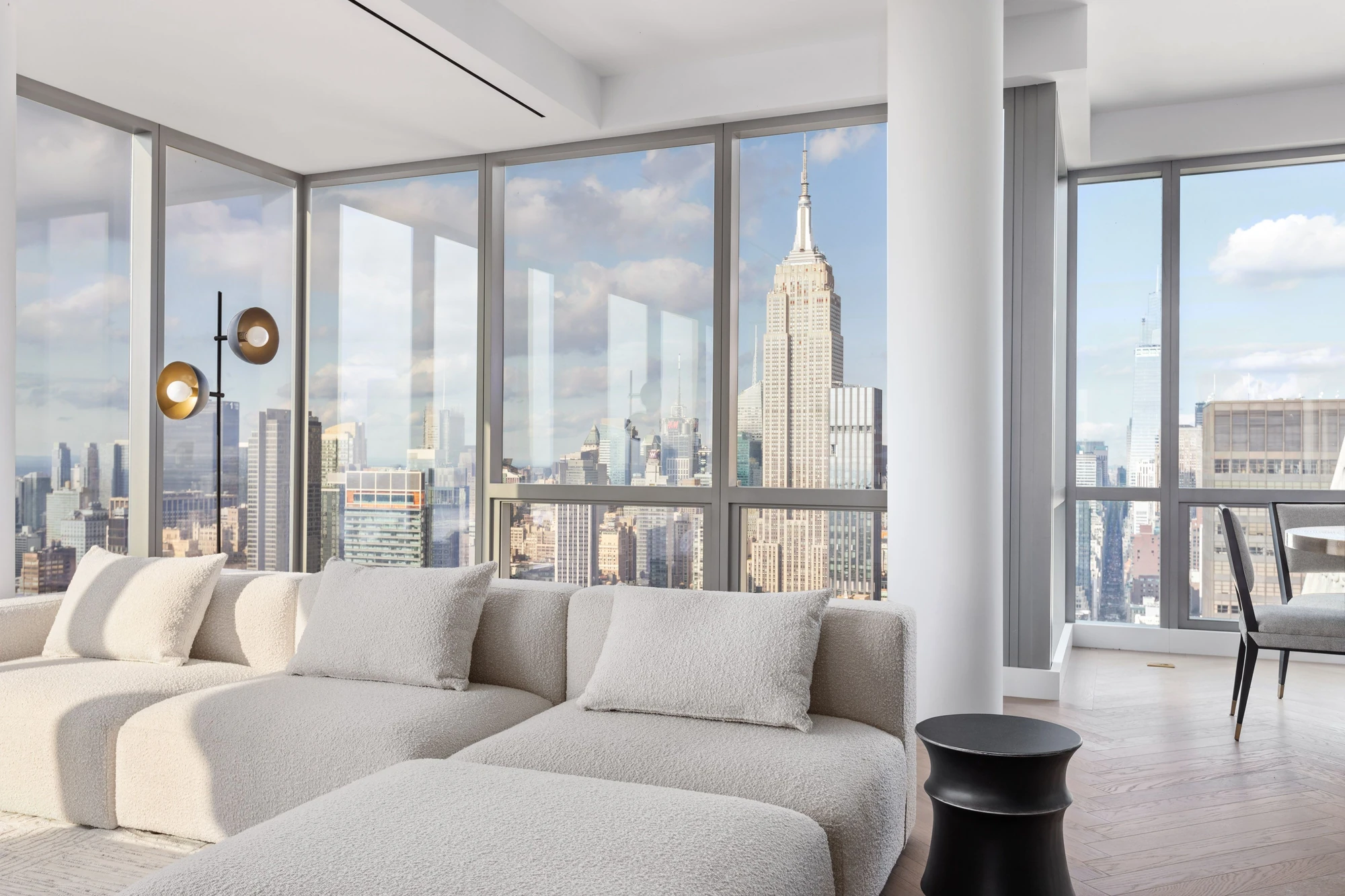 Daylight living-room view with the Empire State Building's crown and spire framed by the windows behind a pale sofa