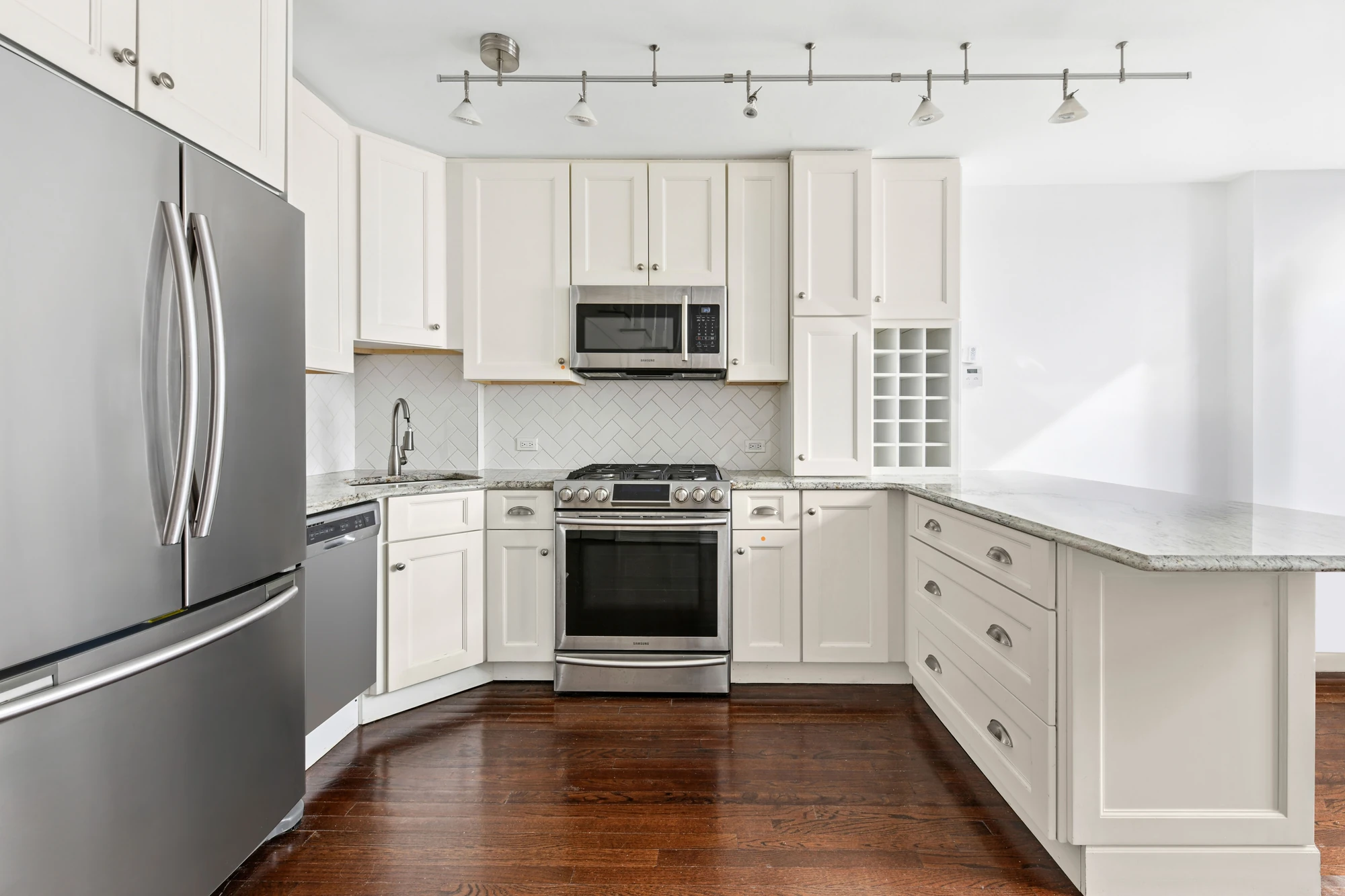 White kitchen cabinetry, stainless steel appliances and a counter open to the living area at 21 South End Avenue #207