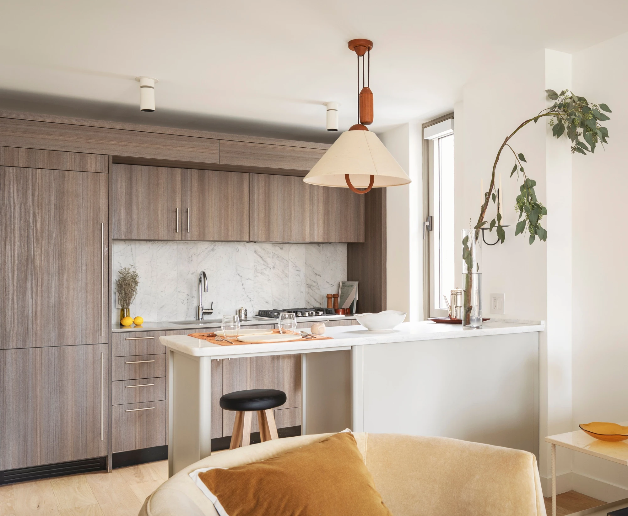 Wood kitchen cabinetry, a veined marble backsplash and an island beside the living area at The Perrie, 234 East 46th Street #701