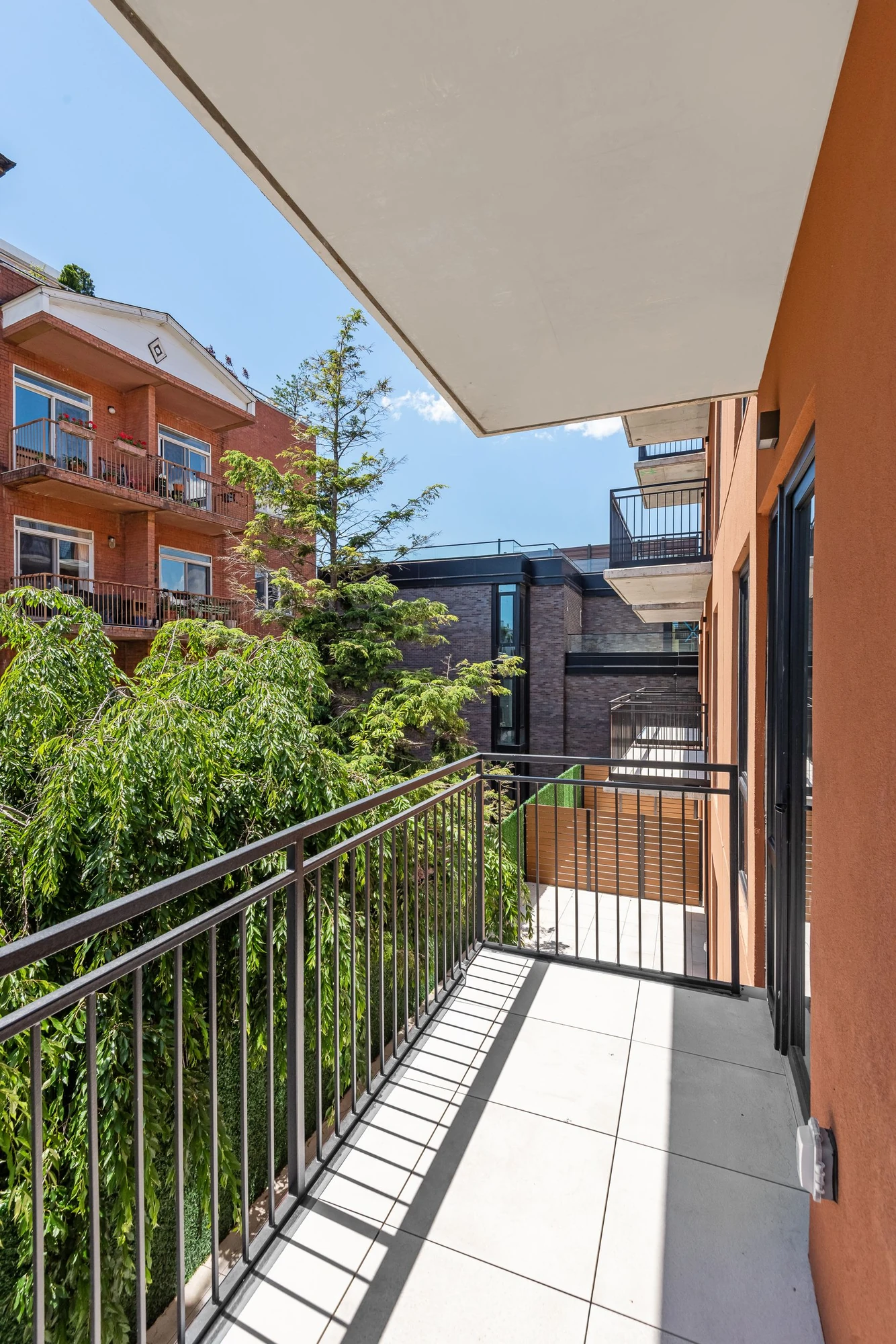 Tiled private balcony with a black railing, neighboring brick buildings and trees at 222 16th Street #4C