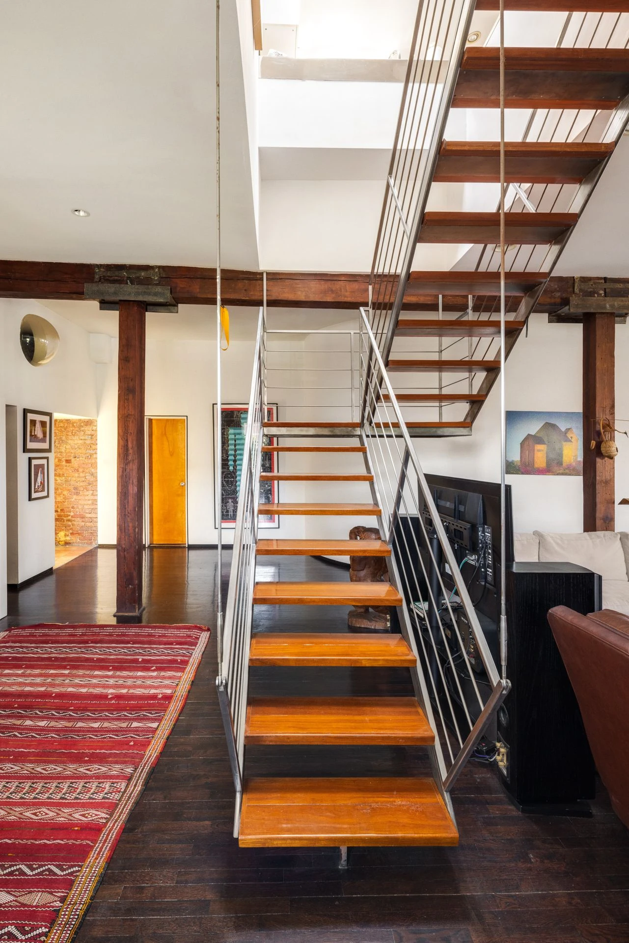 Wood-and-metal open staircase rising toward a bright ceiling opening beside a large wood column and exposed beam