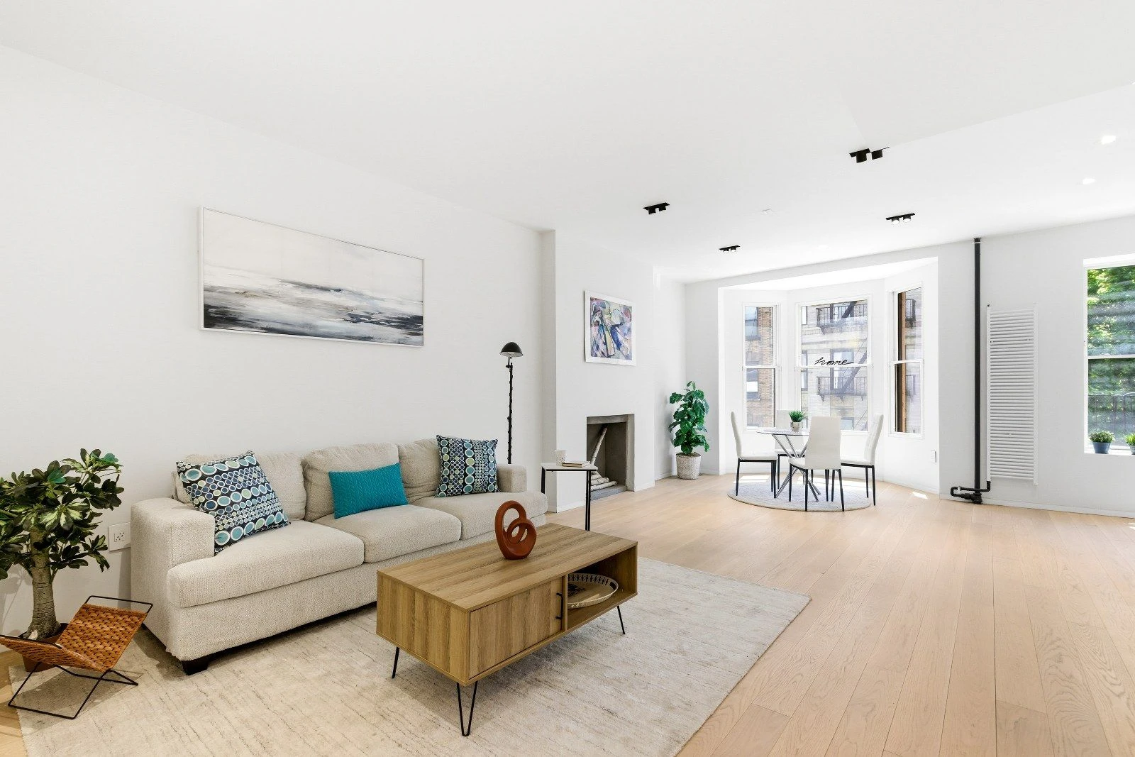 Long living room with a sofa, pale wood floors and dining space beside the windows at 205 East 124th Street #3BC