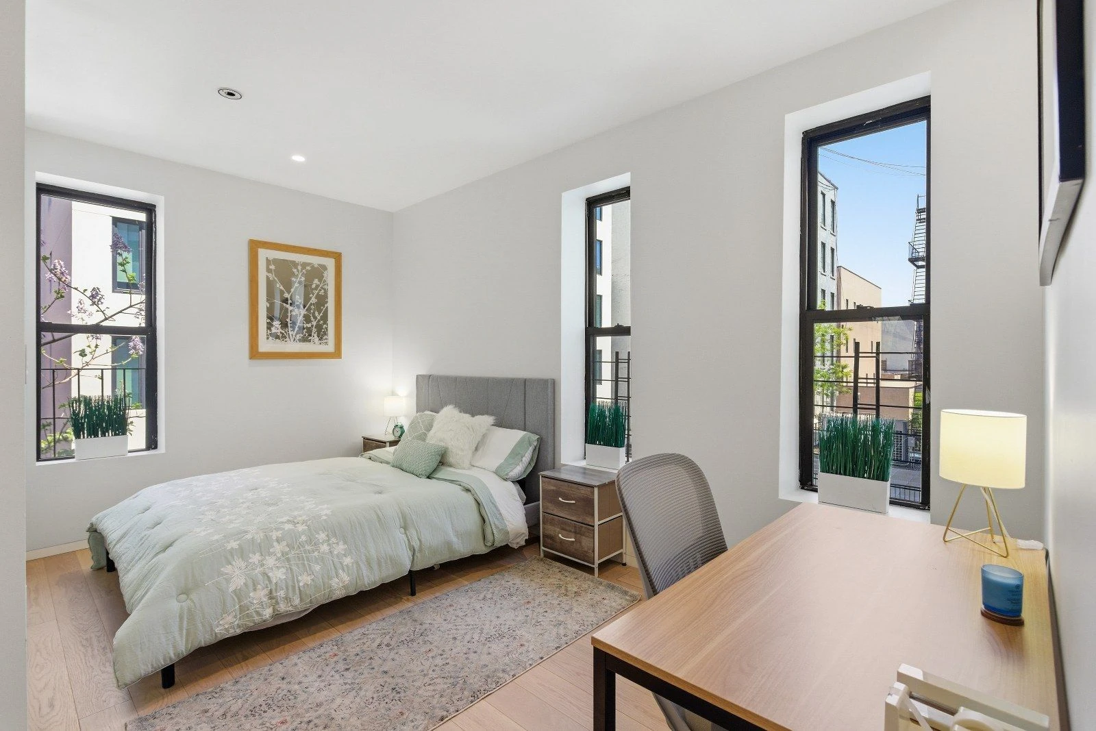 Bedroom with wood floors, two windows and space for a desk at 205 East 124th Street #3BC