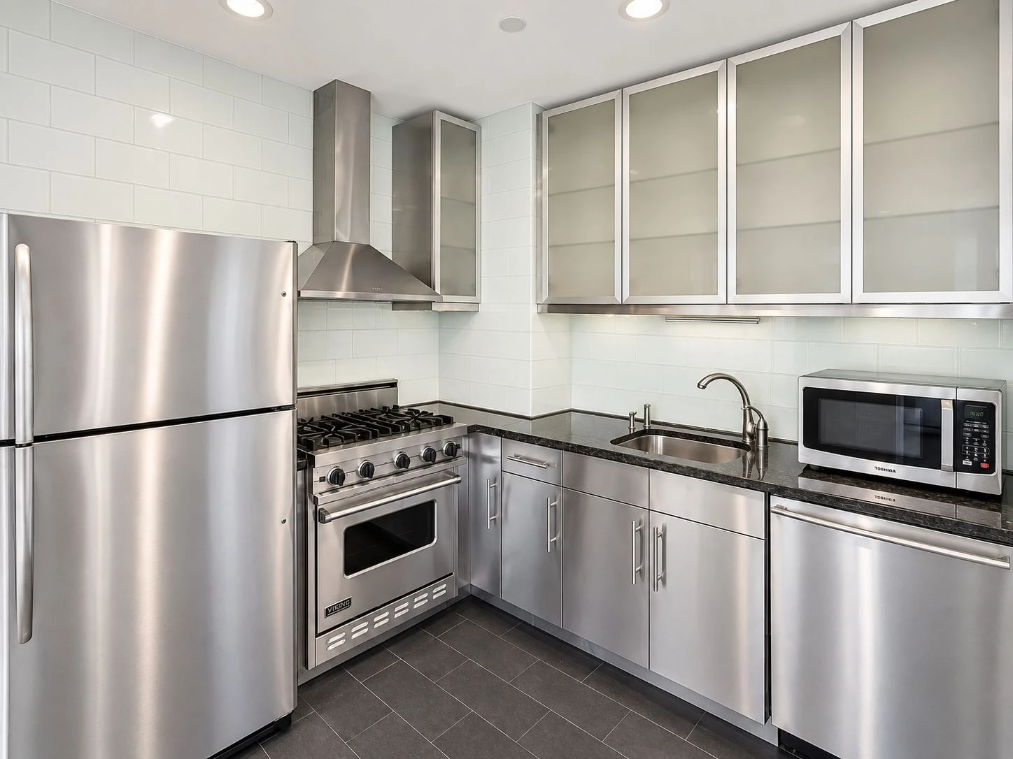 Vacant kitchen with stainless steel appliances, pale cabinetry and a dark counter at 197 Bridge Street #8C