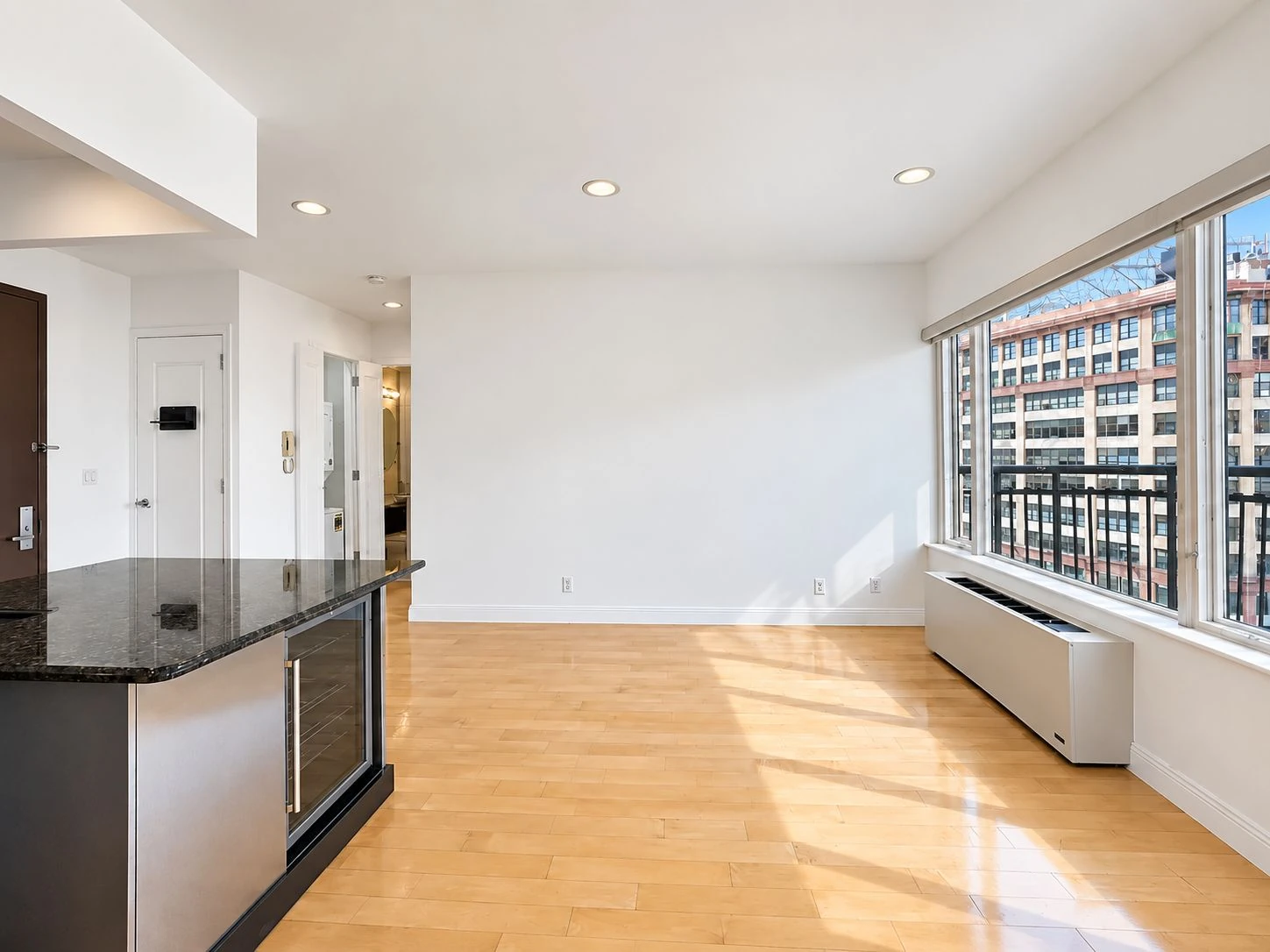 Vacant living room with light wood floors, a kitchen peninsula and balcony windows at 197 Bridge Street #8C